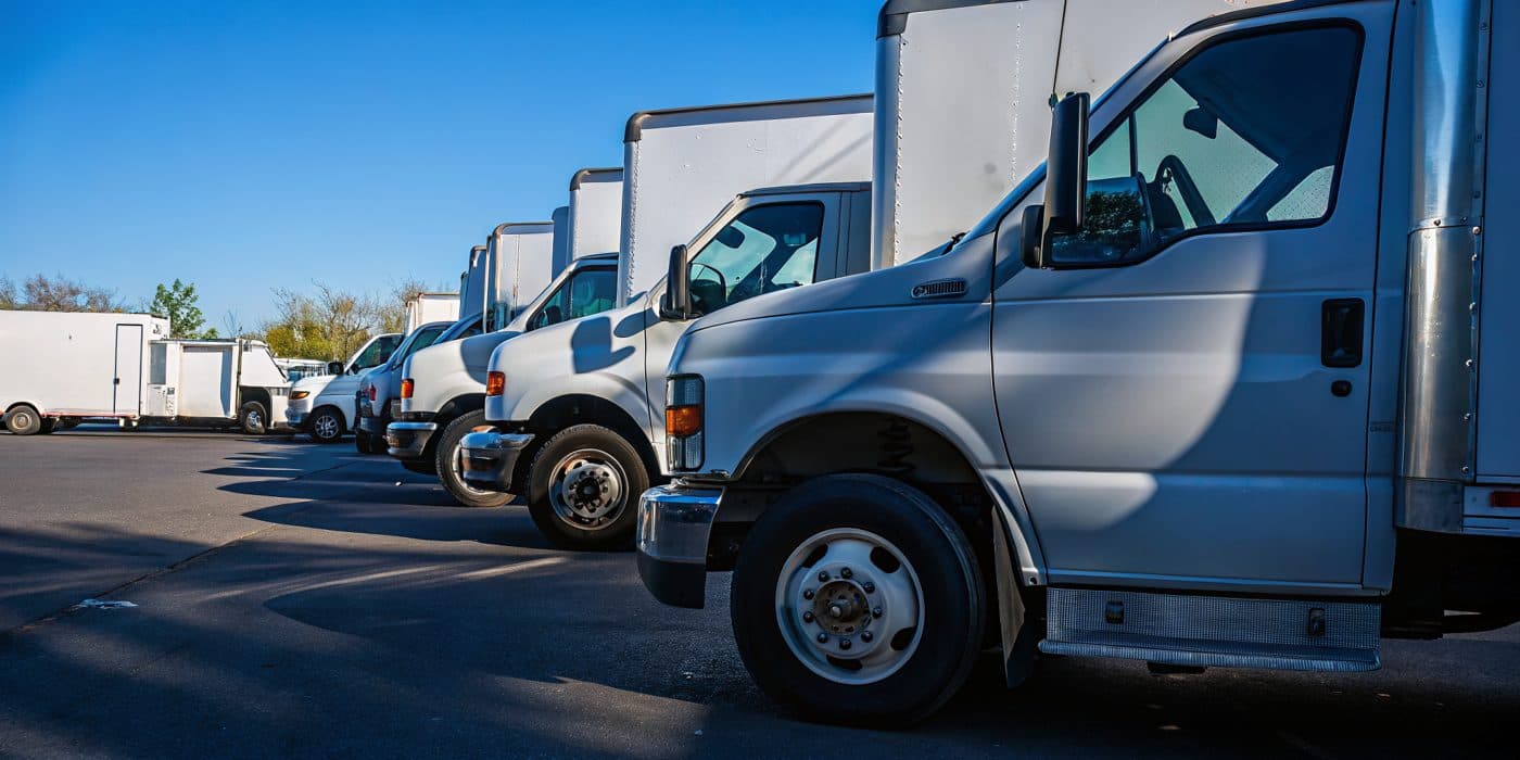 A row of white fleet trucks and vans parked at a depot
